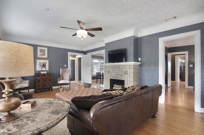 Living area featuring a fireplace, wood finished floors, a textured ceiling, visible vents, and ceiling fan | Image 25
