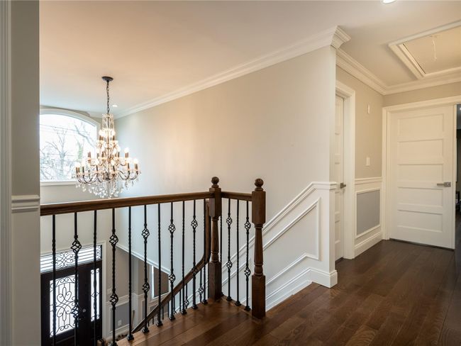 Hallway featuring dark wood-style floors, an upstairs landing, crown molding, attic access, and a notable chandelier | Image 21