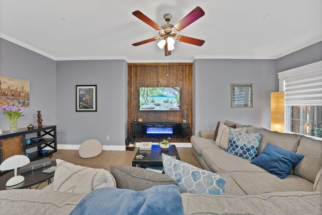 Living room with ornamental molding, a ceiling fan, wood finished floors, baseboards, and a fireplace | Image 21