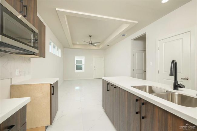 Kitchen featuring stainless steel microwave, a sink, light marble finish flooring, light countertops, and a ceiling fan | Image 10