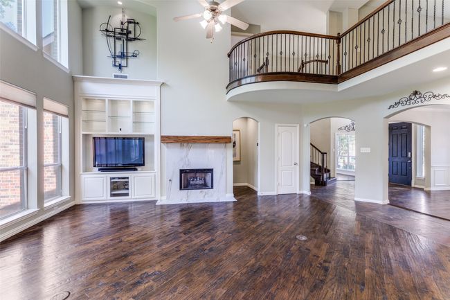 Unfurnished living room with a high ceiling, stairs, a ceiling fan, a fireplace, and arched walkways | Image 4