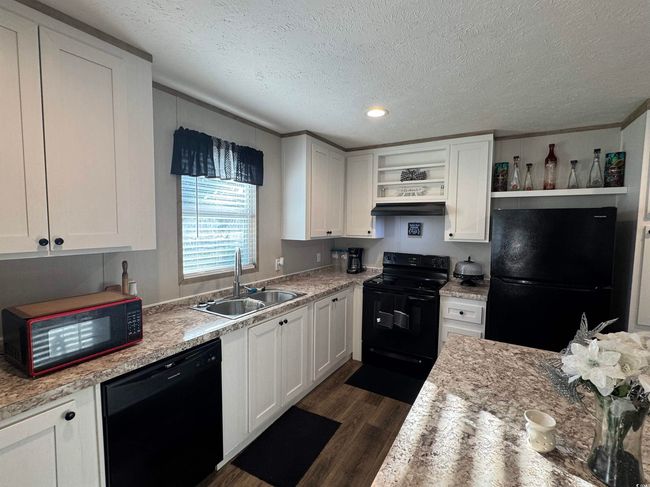Kitchen featuring black appliances, open shelves, dark wood finished floors, white cabinets, and a textured ceiling | Image 6