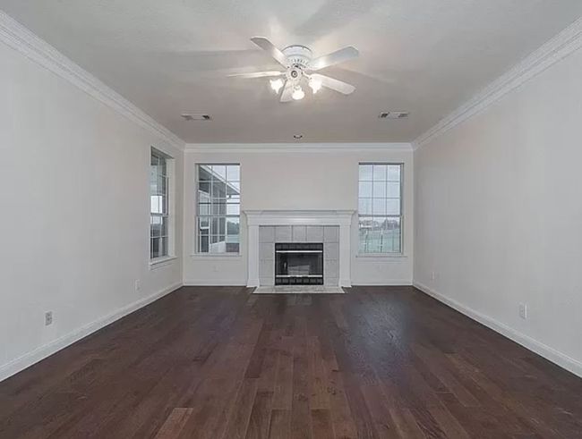 Unfurnished living room with ceiling fan, healthy amount of natural light, dark wood finished floors, and crown molding | Image 10