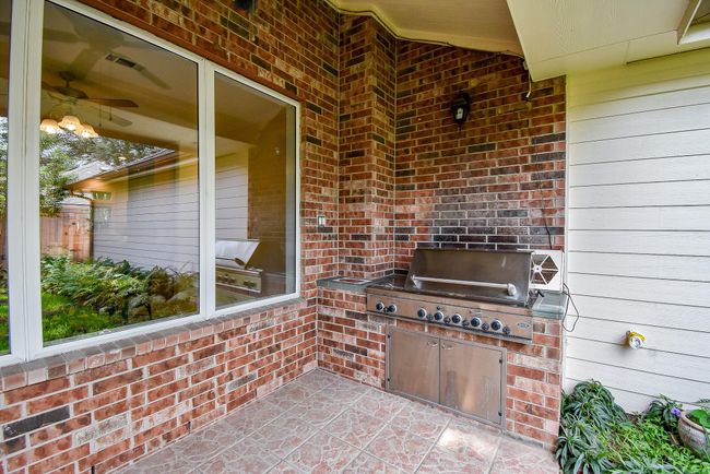 This outdoor space features a built-in stainless steel grill set against a brick wall, perfect for entertaining. The area is covered and adjacent to a large window, providing a cozy and functional barbecue area. | Image 45