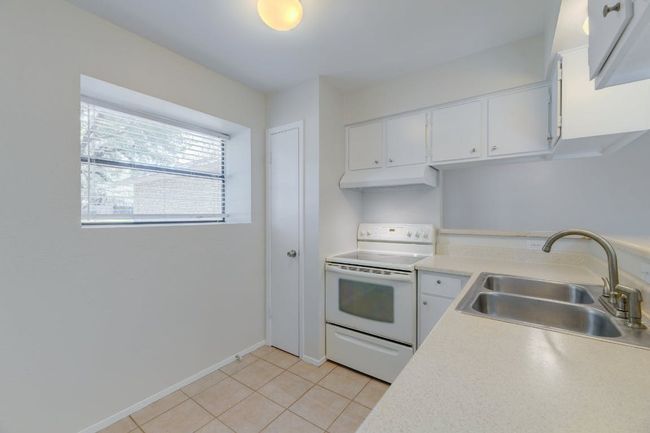 Kitchen with electric stove, a sink, under cabinet range hood, and light countertops | Image 7