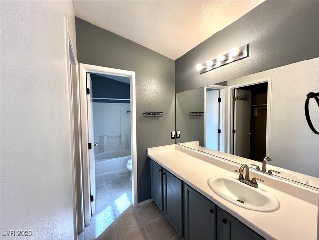 Full bath featuring a textured ceiling, toilet, vanity, shower / tub combination, and tile patterned flooring | Image 13