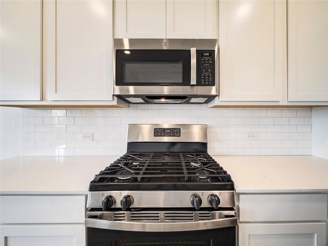Kitchen with appliances with stainless steel finishes, light countertops, decorative backsplash, and white cabinets | Image 9