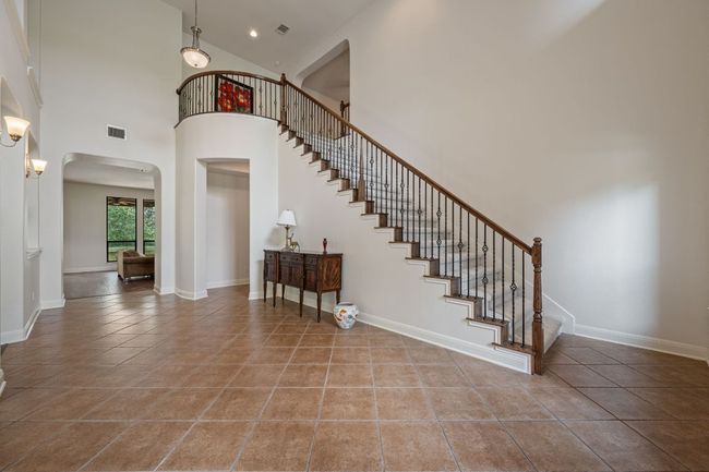 Staircase with tile patterned flooring, a towering ceiling, arched walkways, and visible vents | Image 4