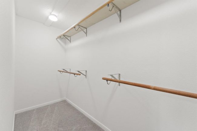 This is a spacious walk-in closet with white walls, carpeted flooring, and ample wooden shelving and hanging space for clothing storage. | Image 21