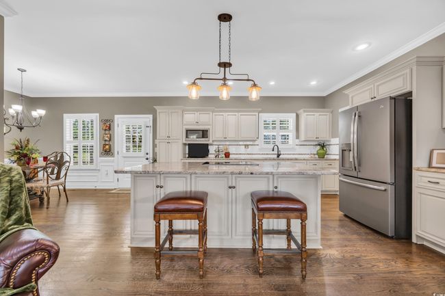 Kitchen with appliances with stainless steel finishes, a chandelier, a kitchen breakfast bar, dark wood-type flooring, and ornamental molding | Image 8
