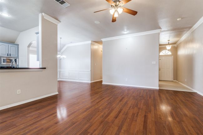 Unfurnished living room featuring a ceiling fan, dark wood-style floors, crown molding, arched walkways, and lofted ceiling | Image 7