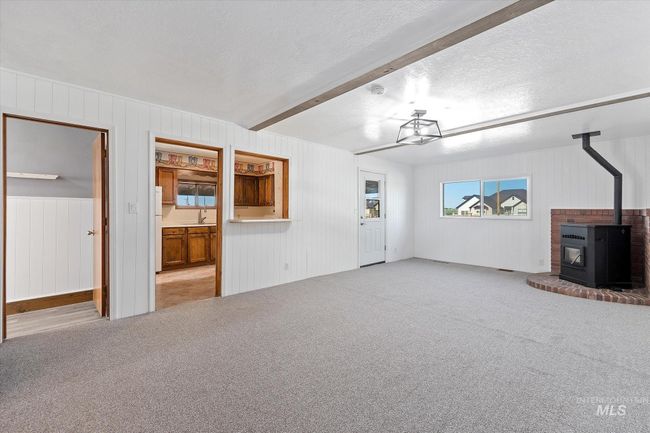 Unfurnished living room featuring a wood stove, a textured ceiling, carpet floors, wood walls, and beamed ceiling | Image 7