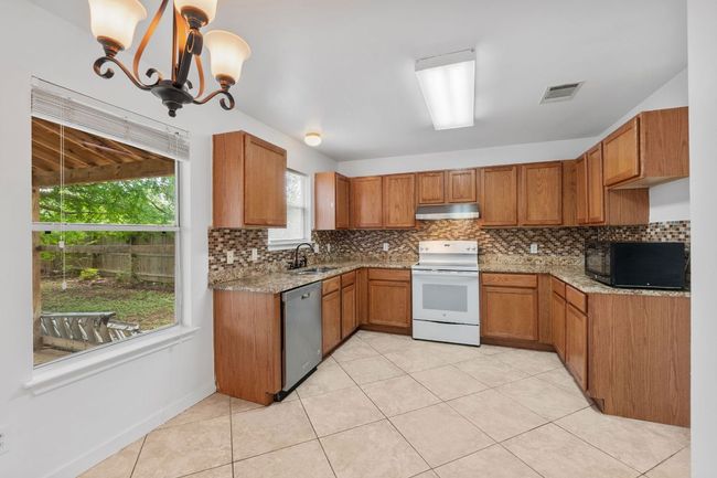 Kitchen featuring white electric stove, black microwave, under cabinet range hood, a sink, and dishwasher | Image 12