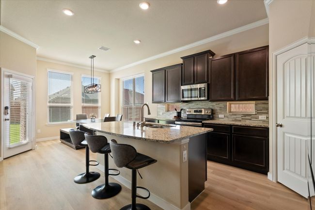 Kitchen featuring appliances with stainless steel finishes, a sink, light wood-type flooring, a kitchen breakfast bar, and tasteful backsplash | Image 19