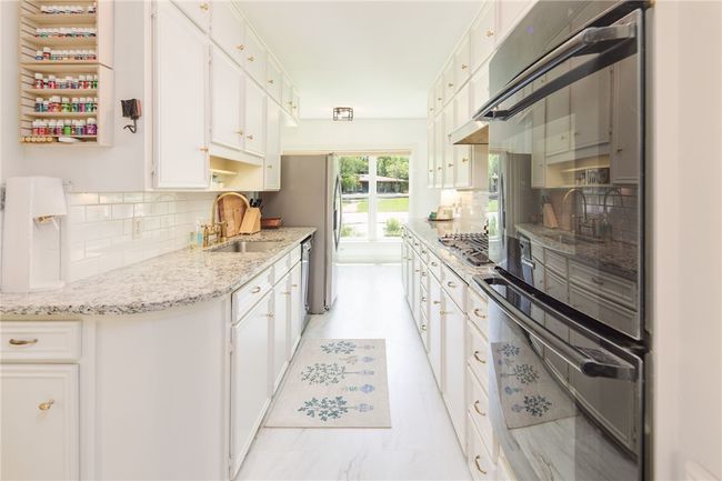 Kitchen featuring a sink, decorative backsplash, stainless steel gas cooktop, and white cabinets | Image 11