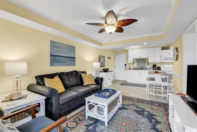Living room with light tile patterned flooring, a tray ceiling, crown molding, and a ceiling fan | Image 13