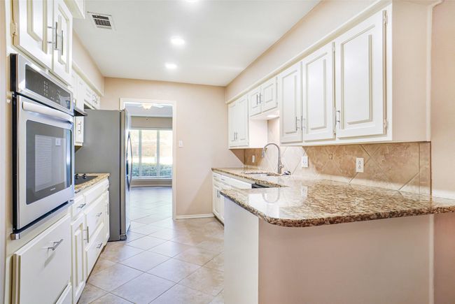 Kitchen with stainless steel appliances, a sink, white cabinetry, backsplash, and a peninsula | Image 5