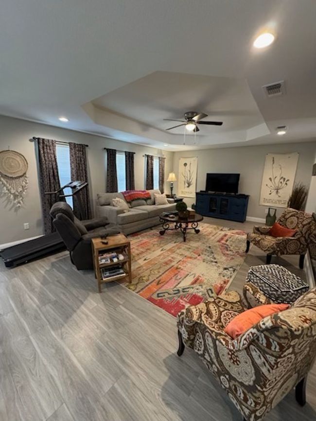Living room featuring a tray ceiling, baseboards, ceiling fan, and wood finished floors | Image 16