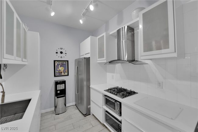 Kitchen featuring stainless steel appliances, range hood, white cabinets, light countertops, and glass insert cabinets | Image 12
