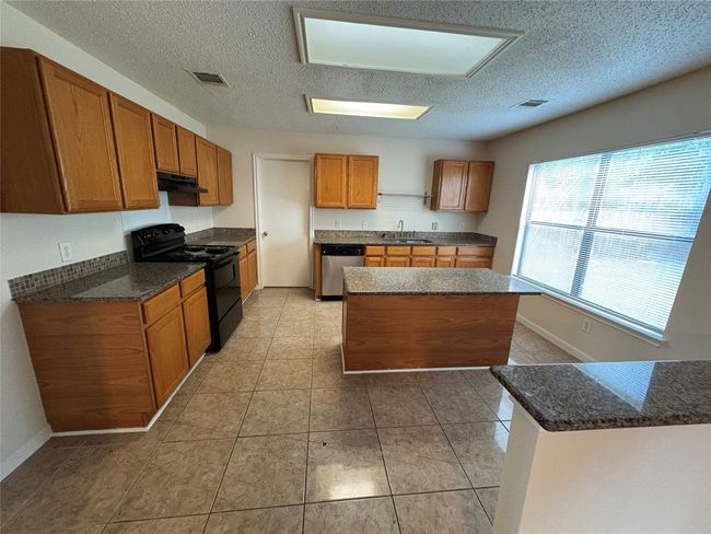 Kitchen featuring black electric range, a textured ceiling, brown cabinets, dishwasher, and a center island | Image 7