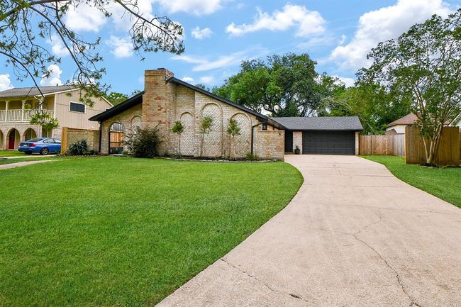 This photo showcases a charming single-story brick home with a modern, dark garage door. The property features a spacious driveway, well-maintained lawn, and mature trees, offering a welcoming curb appeal in a suburban neighborhood. | Image 6