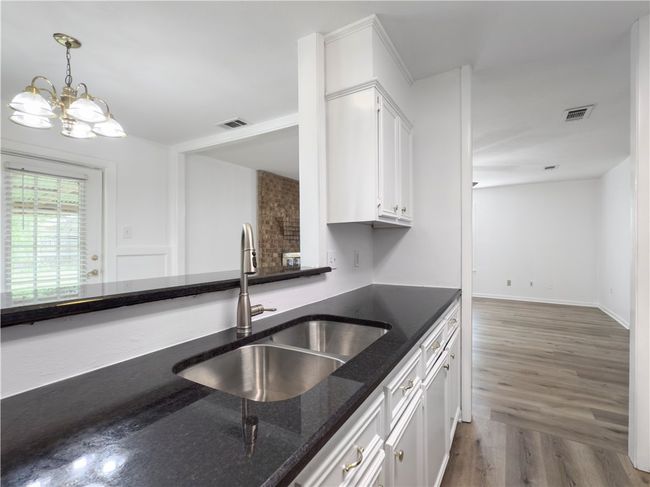 Kitchen with dark stone countertops, white cabinets, decorative light fixtures, wood finished floors, and a chandelier | Image 7