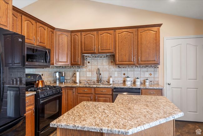 Kitchen with vaulted ceiling, a sink, light stone countertops, tasteful backsplash, and black appliances | Image 12