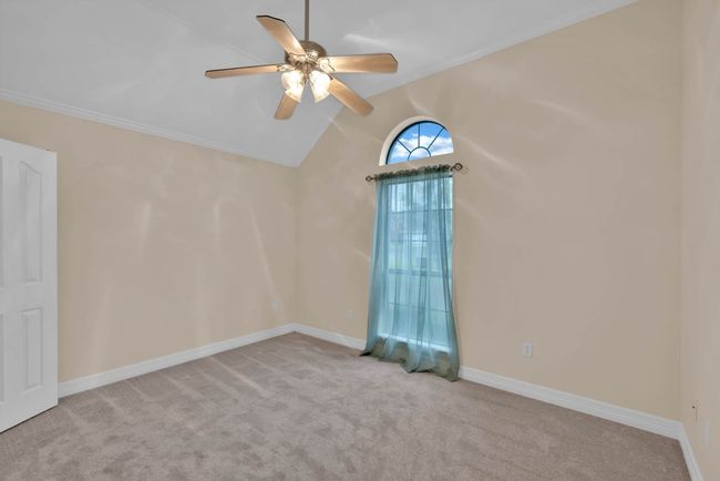 Carpeted empty room featuring a ceiling fan, vaulted ceiling, and ornamental molding | Image 23