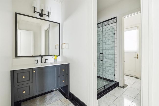 Blending luxury with practicality, this beautifully appointed first-floor en-suite has direct access to the backyard, making it perfect as a pool bath. It features polished Carrara marble tile in a farmhouse stone pattern, sleek honed quartz countertops, custom cabinetry, and a generously sized glass-enclosed walk-in shower. | Image 31