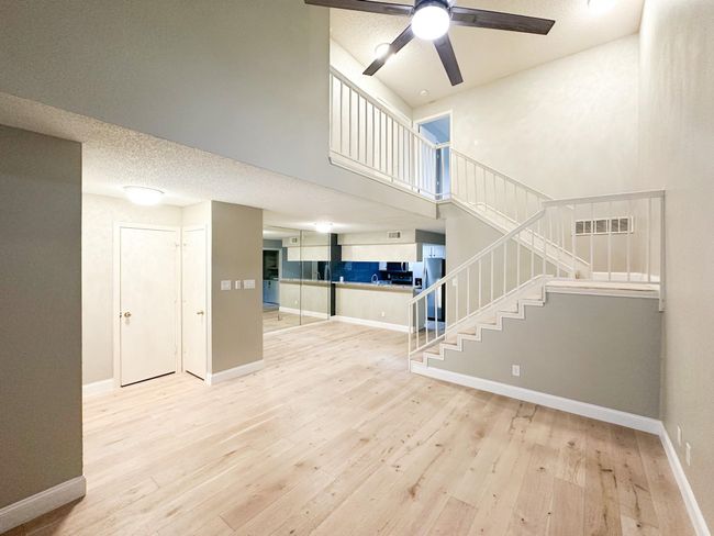 Unfurnished living room with a high ceiling, stairs, wood finished floors, a ceiling fan, and baseboards | Image 4