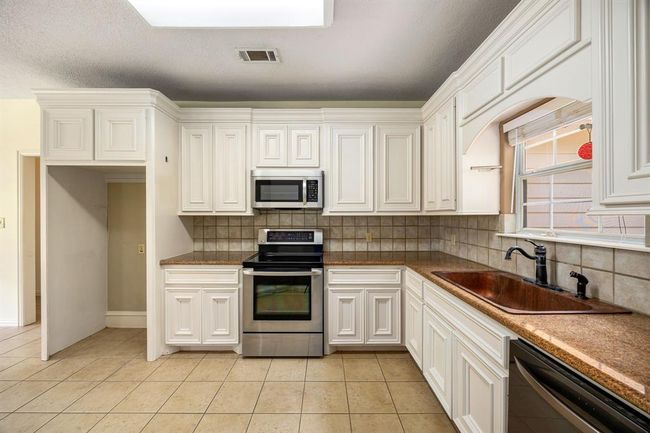 This cozy kitchen has beautiful white custom cabinetry and a bronze sink that overlooks the front yard. | Image 12