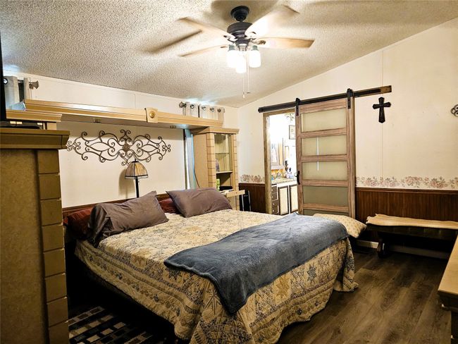 Bedroom with a textured ceiling, a barn door, dark wood-type flooring, a wainscoted wall, and vaulted ceiling | Image 10