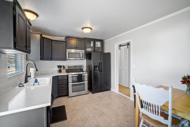 Kitchen featuring appliances with stainless steel finishes, a sink, light countertops, tasteful backsplash, and crown molding | Image 5