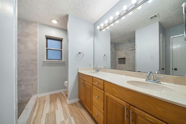 Ensuite bath features a double-sink vanity with generous cabinet storage and a large wall mirror. Spacious walk-in shower includes updated tile and built-in shelving. | Image 21