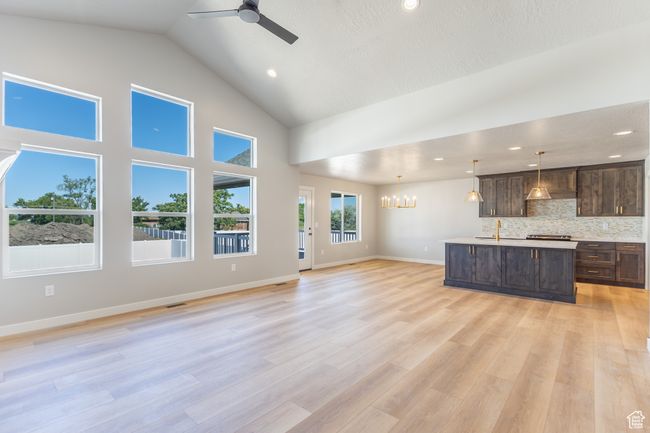Unfurnished living room with a chandelier, a ceiling fan, high vaulted ceiling, light wood finished floors, and recessed lighting | Image 15