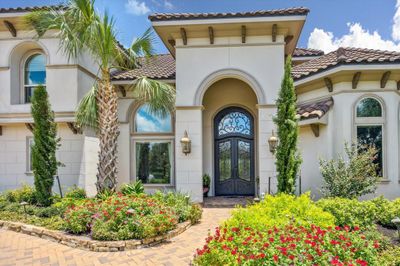 There is a double iron and glass front door with extended transom window over the door, to let in lots of natural light into the foyer. The extensive tropical landscaping is colorful and beautiul. Ther is a covered front patio with room enough for a bench and flowring pots. | Image 3