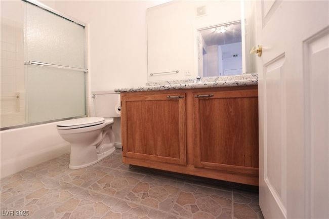 Full bath featuring stone floors, toilet, vanity, and enclosed tub / shower combo | Image 16