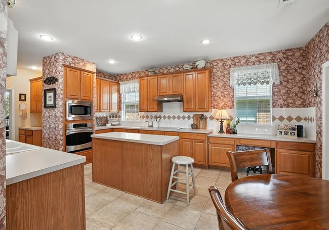Kitchen featuring stainless steel appliances, under cabinet range hood, a center island, light countertops, and backsplash | Image 11