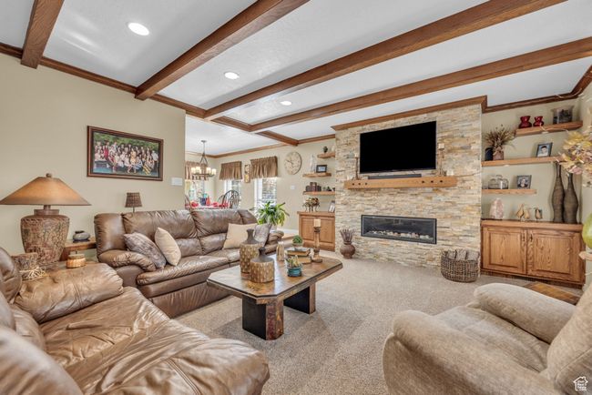 Living room featuring beam ceiling, a chandelier, ornamental molding, carpet, and a stone fireplace | Image 6