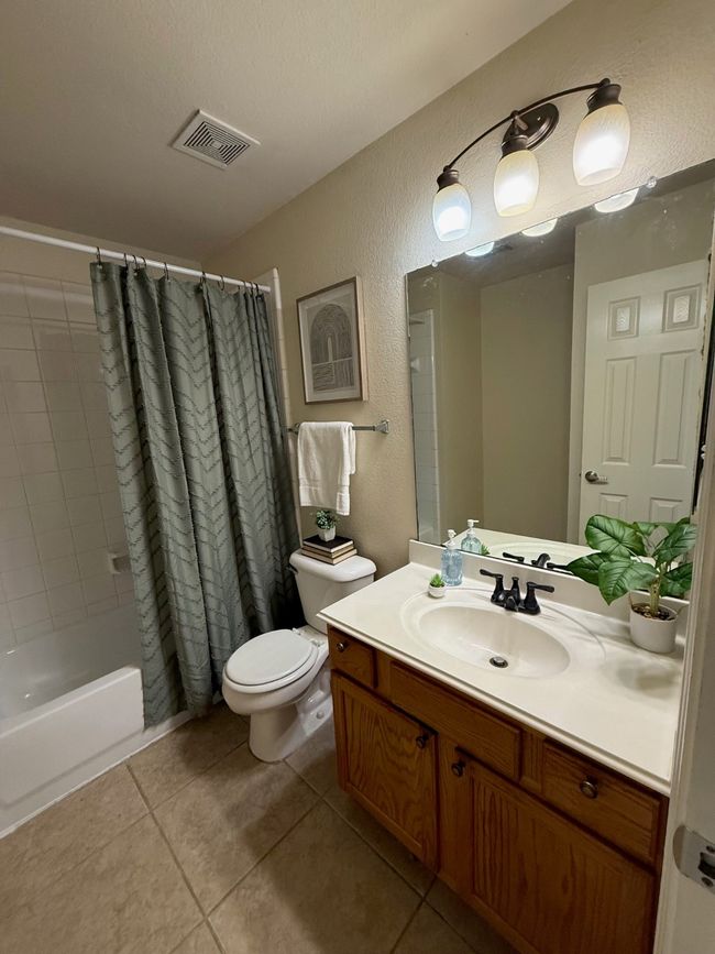 Bathroom with a textured wall, tile patterned floors, vanity, toilet, and shower / bath combo | Image 19