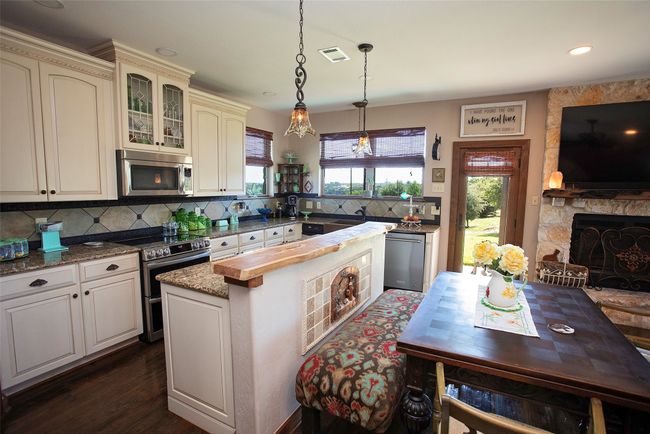Kitchen featuring appliances with stainless steel finishes, tasteful backsplash, cream cabinetry, a fireplace, and glass insert cabinets | Image 19