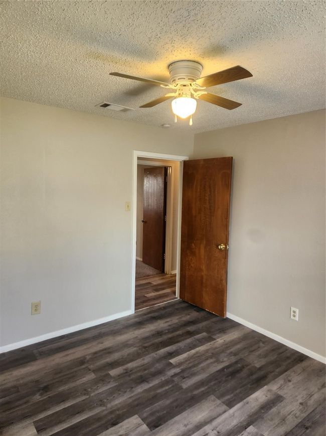 Empty room with ceiling fan, a textured ceiling, dark wood-type flooring, and baseboards | Image 16