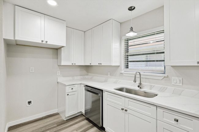 Kitchen featuring stainless steel dishwasher, light stone counters, light wood-style floors, a sink, and white cabinetry | Image 17