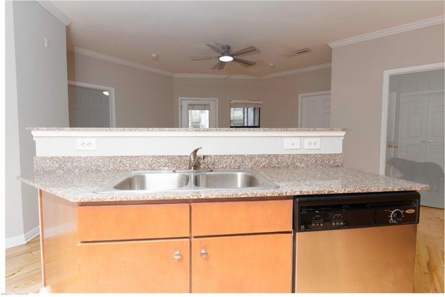 Kitchen with stainless steel dishwasher, light wood-style flooring, crown molding, a ceiling fan, and light stone counters | Image 13