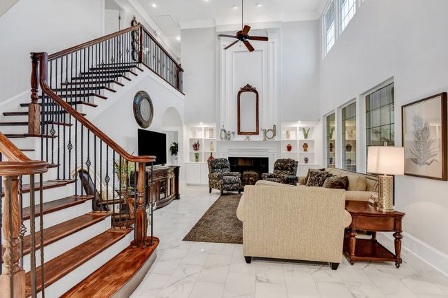 Living area with light marble finish flooring, a high ceiling, a fireplace, ceiling fan, and built in features | Image 8