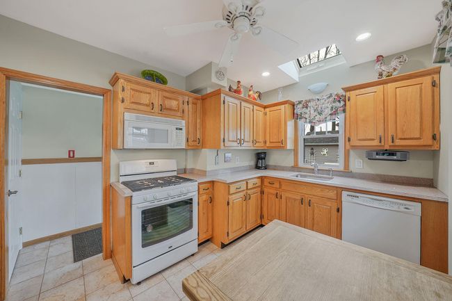 Kitchen featuring light countertops, a sink, a skylight, white appliances, and visible vents | Image 10