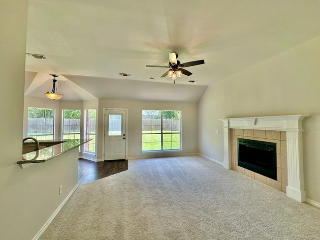 Unfurnished living room featuring dark carpet, a ceiling fan, lofted ceiling, and a fireplace | Image 21