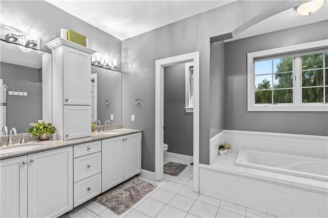 Full bath with double vanity, a bath, toilet, tile patterned flooring, and baseboards | Image 21