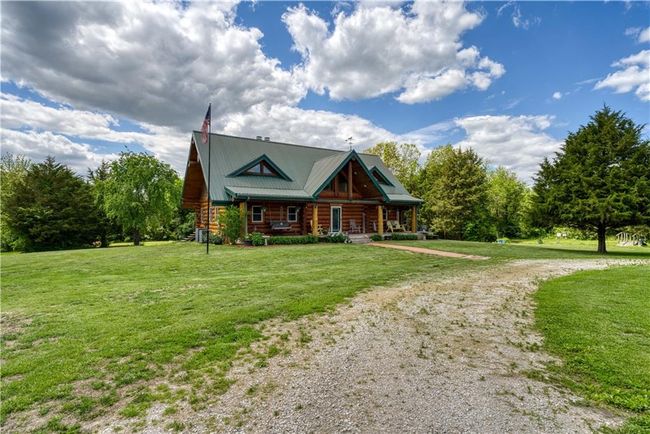 Log-style house featuring covered porch, log siding, metal roof, a front lawn, and gravel driveway | Image 4