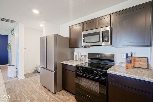 kitchen with appliances with stainless steel finishes, dark brown cabinets, light wood-type flooring, light stone countertops, and recessed lighting | Image 15